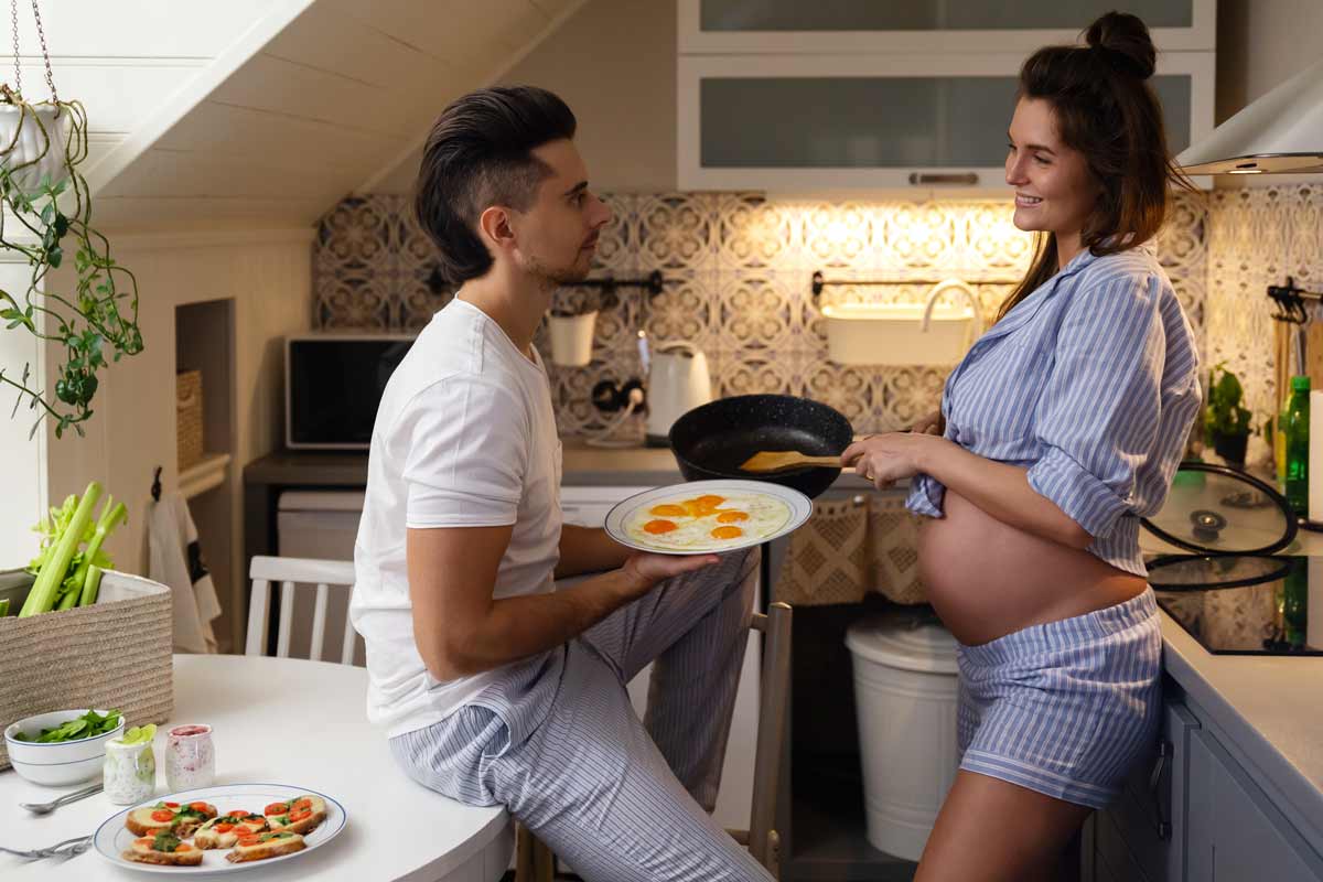 Donna incinta fa colazione con uova fritta.